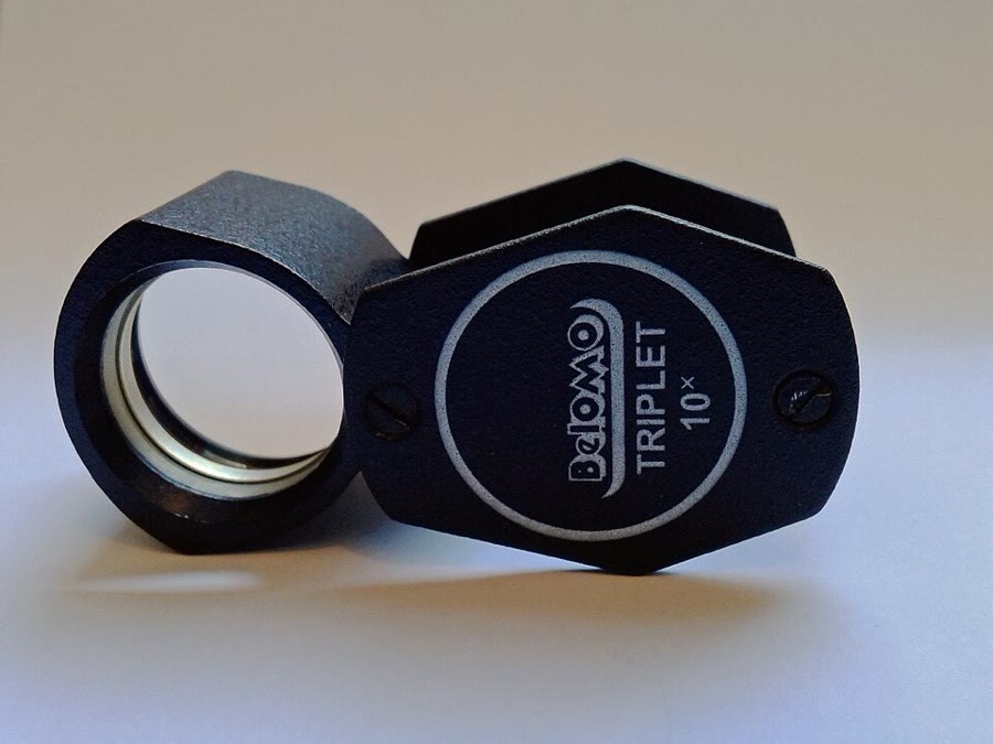 A black folding hand lens with TRIPLET 10X printed on its case